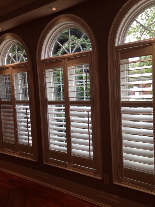 White shutters on arched windows in a wood-trimmed room