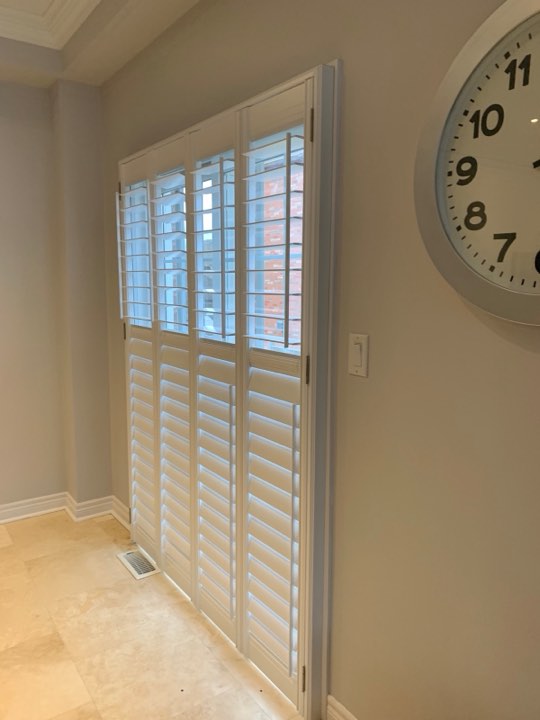 White shutters on a tall window beside a wall clock
