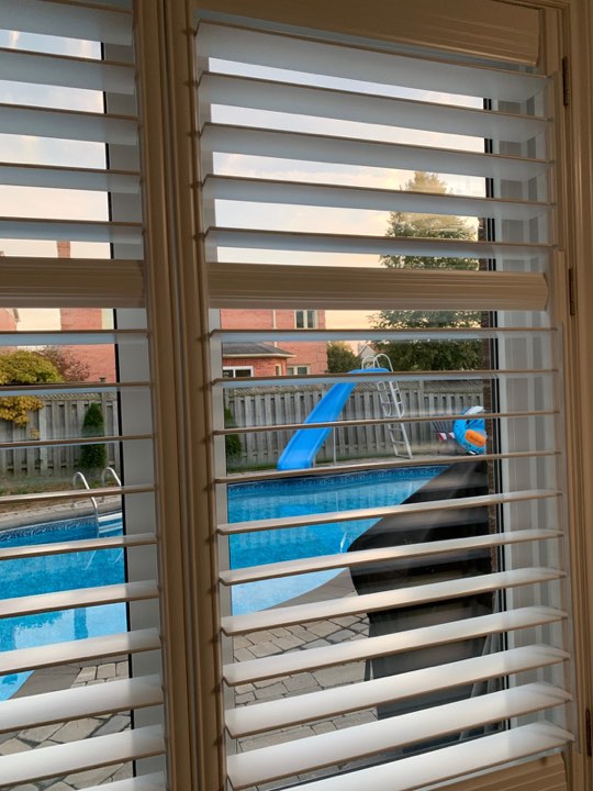 Close-up of open shutter louvres looking out to a backyard pool